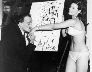 Salvador Dali and Raquel Welch's hand in front of his abstract portrait of her.